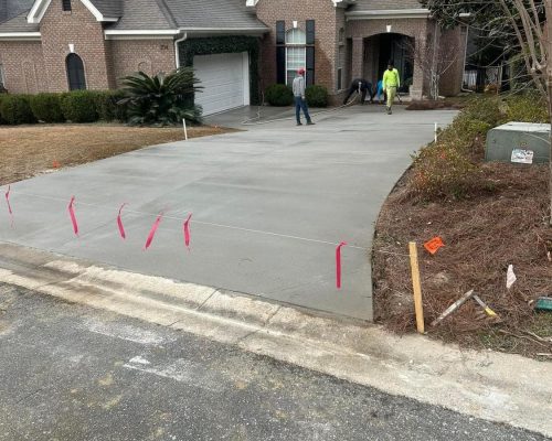 3Concrete driveway construction in Charleston, SC – Workers pouring concrete on a sunny day, with tools and equipment scattered around.